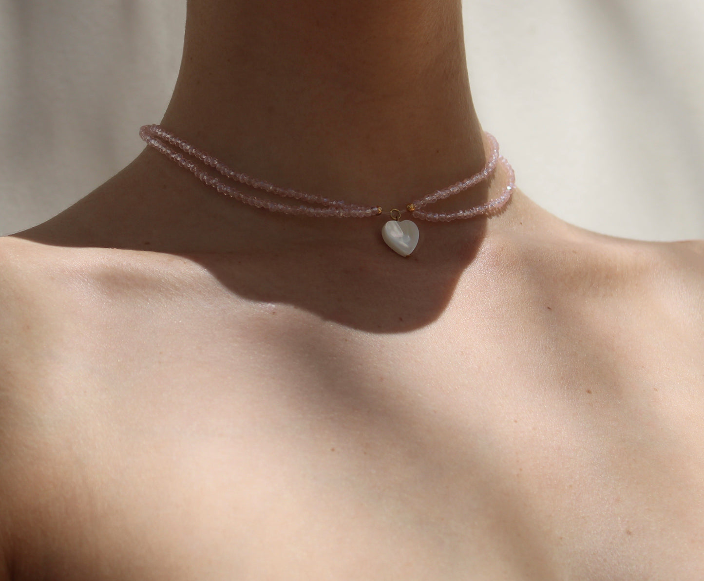 Delicate necklace featuring pink crystal beads measuring 2mm in size, accentuated by a small heart-shaped white shell pendant for a charming touch.
