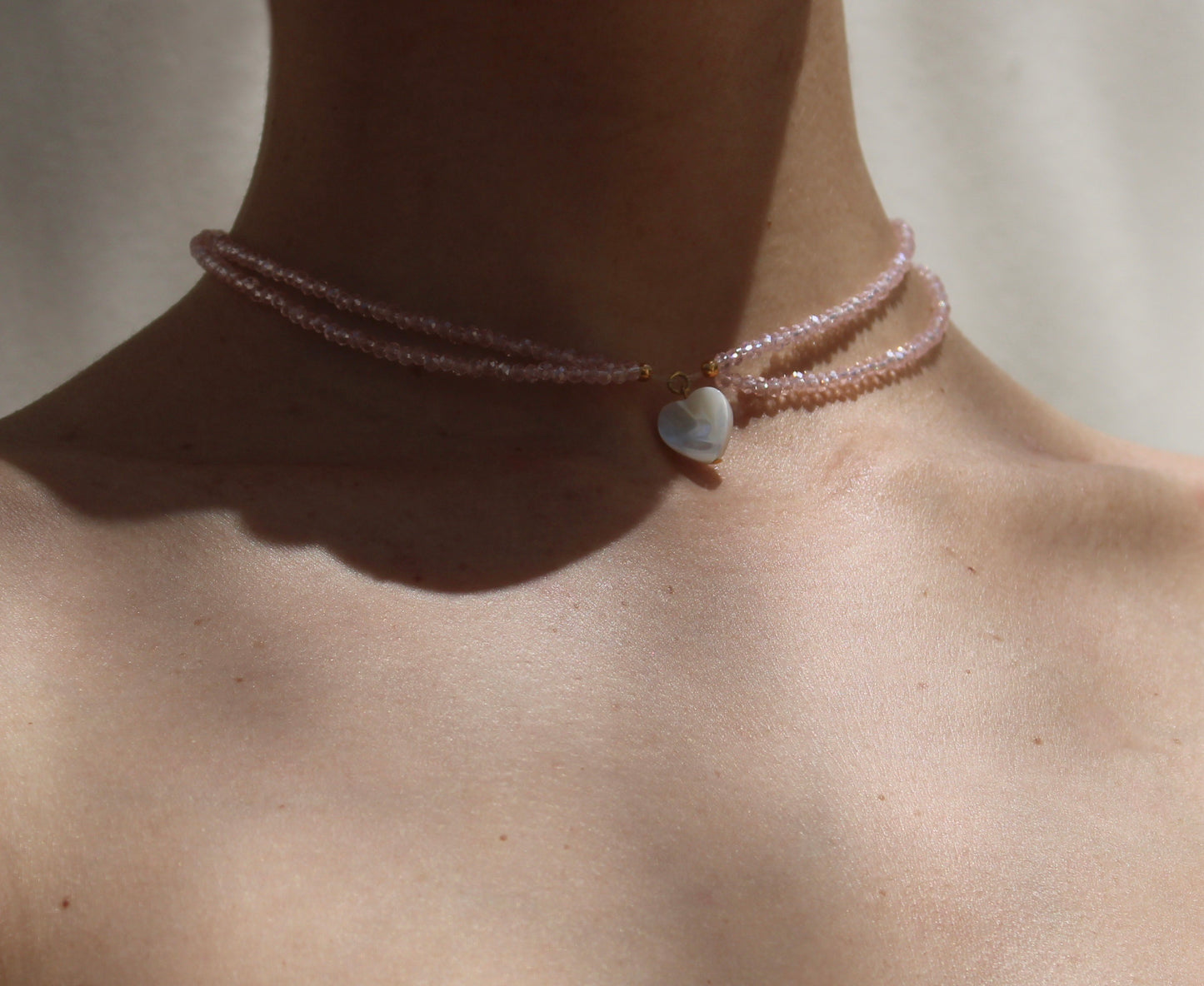 Delicate necklace featuring pink crystal beads measuring 2mm in size, accentuated by a small heart-shaped white shell pendant for a charming touch.