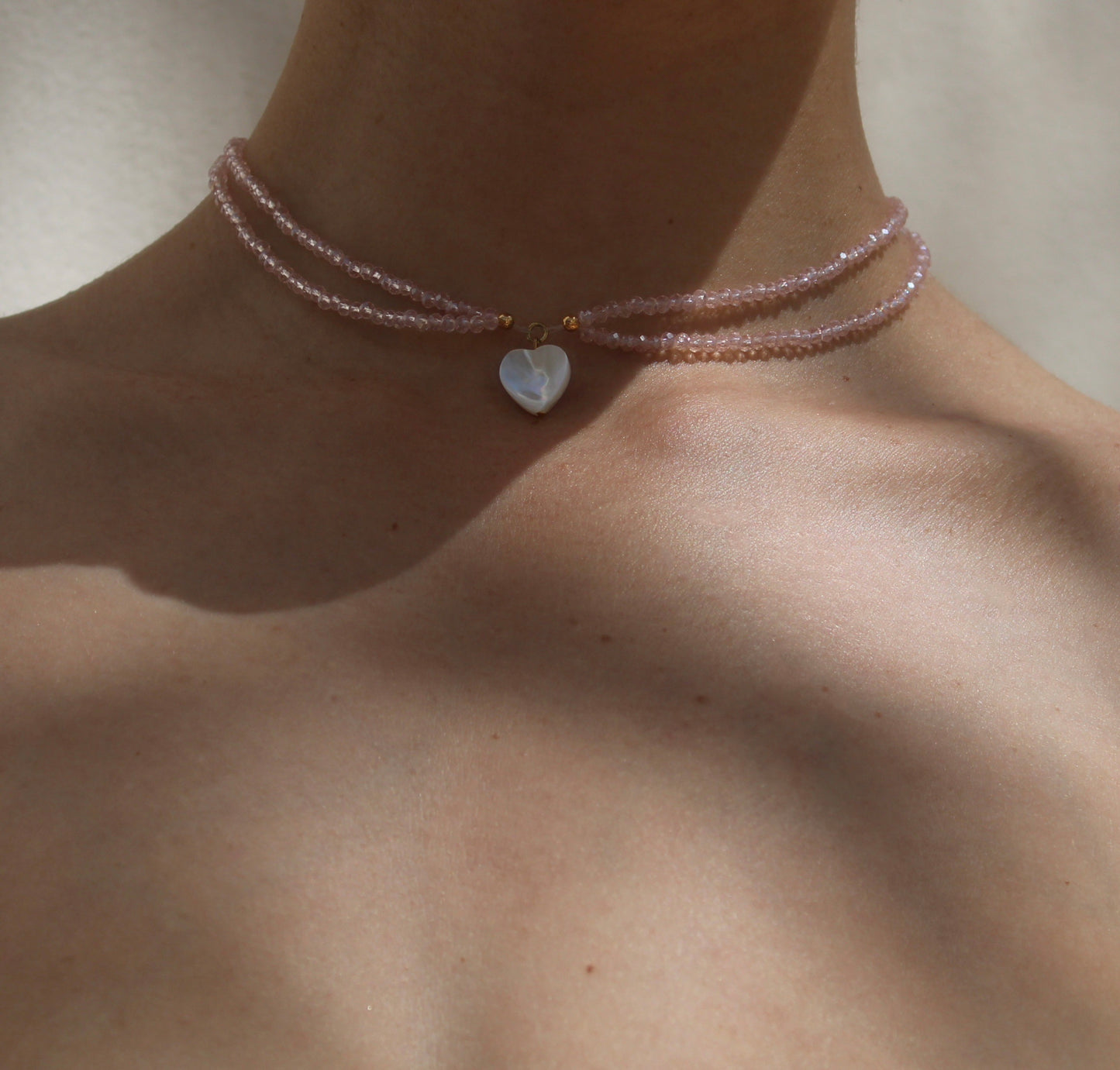 Delicate necklace featuring pink crystal beads measuring 2mm in size, accentuated by a small heart-shaped white shell pendant for a charming touch.